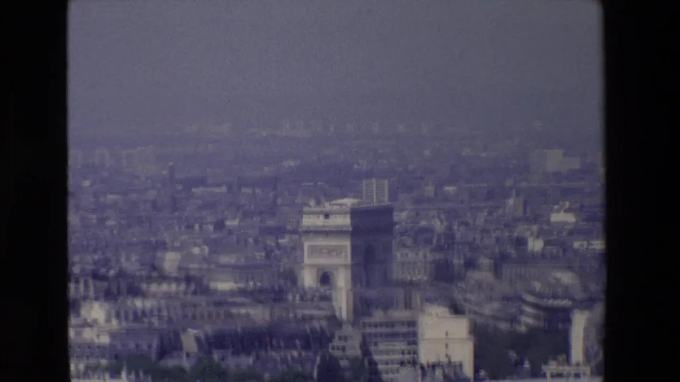 1969 Paris home-movie frame showing the Arc de Triomphe from a high aerial vantage point, surrounded by hazy rooftops and dark 8mm frame borders.