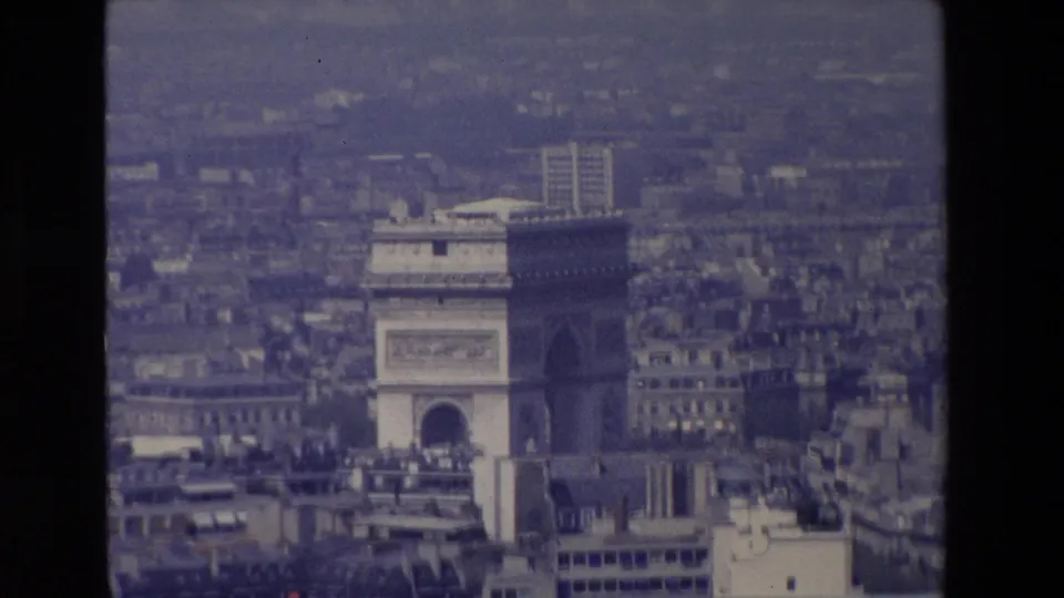 1969 Paris 8mm frame showing the Arc de Triomphe amid dense city blocks, with soft focus and muted archival color.