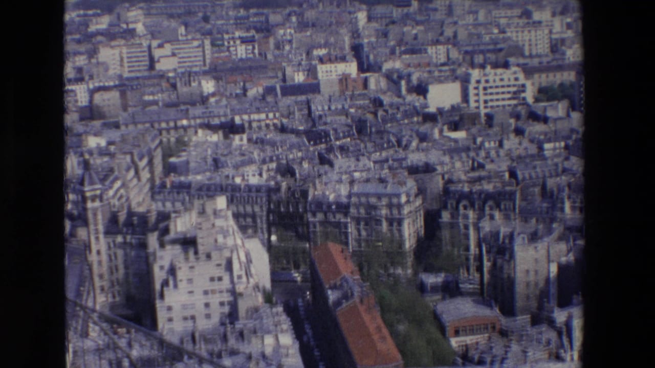 1969 Paris aerial-style home-movie frame with tightly packed buildings, flat rooftops, narrow streets, trees, and a dark vertical obstruction from the filmed vantage or scan.