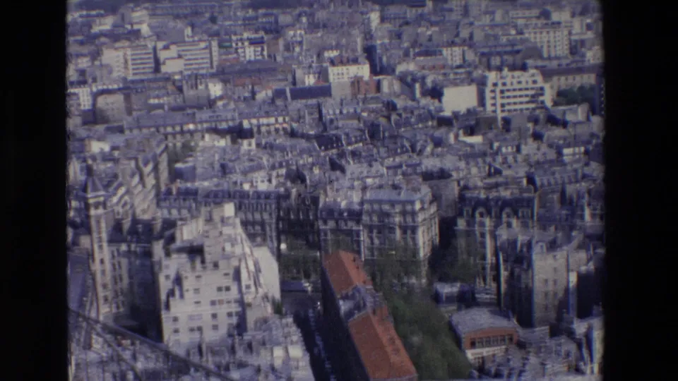 1969 Paris aerial-style home-movie frame with tightly packed buildings, flat rooftops, narrow streets, trees, and a dark vertical obstruction from the filmed vantage or scan.