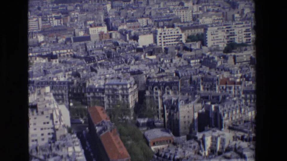 High-angle 1969 Paris city view showing dense apartment rows, mixed roof shapes, street canyons, small green areas, and a prominent reddish roof.