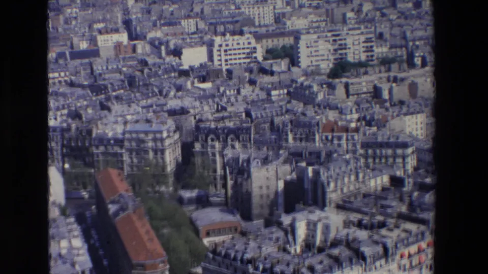 1969 Paris aerial-style frame with dense urban sprawl, pale high-rise and mid-rise buildings, roof patterns, street corridors, and patches of trees.