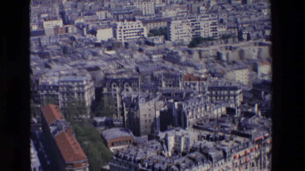 1969 Paris aerial view over Haussmannian apartment blocks, slate rooftops, narrow streets, trees, and larger modern buildings in the background.