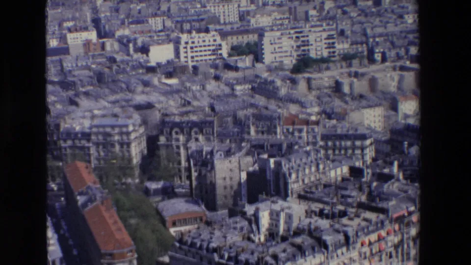 1969 Paris aerial view over Haussmannian apartment blocks, slate rooftops, narrow streets, trees, and larger modern buildings in the background.