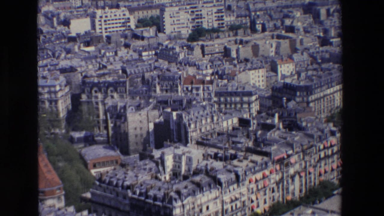 1969 Paris aerial frame showing rows of residential buildings, grey roofs, street gaps, greenery, and mid-century structures beyond the older blocks.