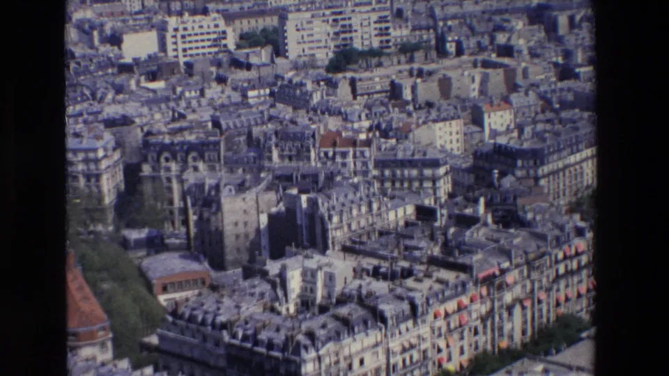 1969 Paris aerial frame showing rows of residential buildings, grey roofs, street gaps, greenery, and mid-century structures beyond the older blocks.