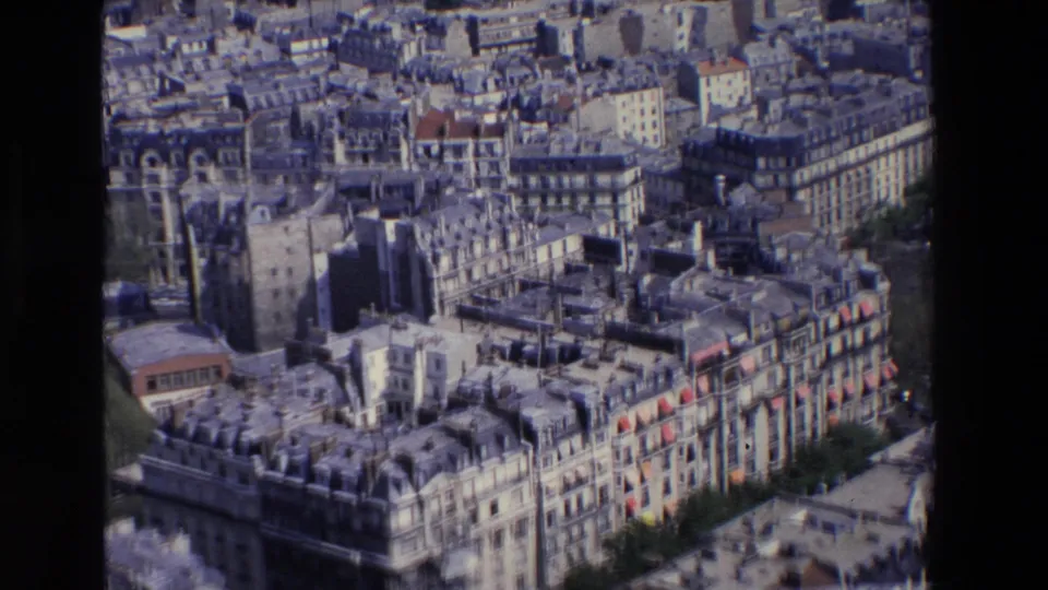 1969 Paris aerial view with foreground Haussmannian facades, red awnings or roof details, rooftop chimneys, and densely packed neighboring buildings.