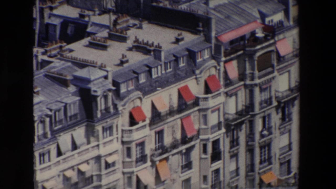 1969 Paris frame of a multi-story residential block with mansard rooftops, dormer windows, ornate facade details, balconies, and several red awnings.