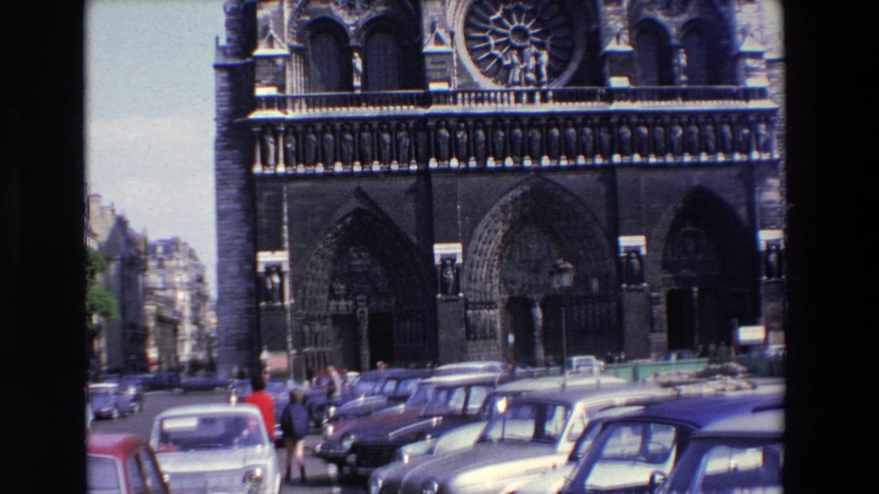 Cathedral entrance and rose window seen over a row of cars and pedestrians.