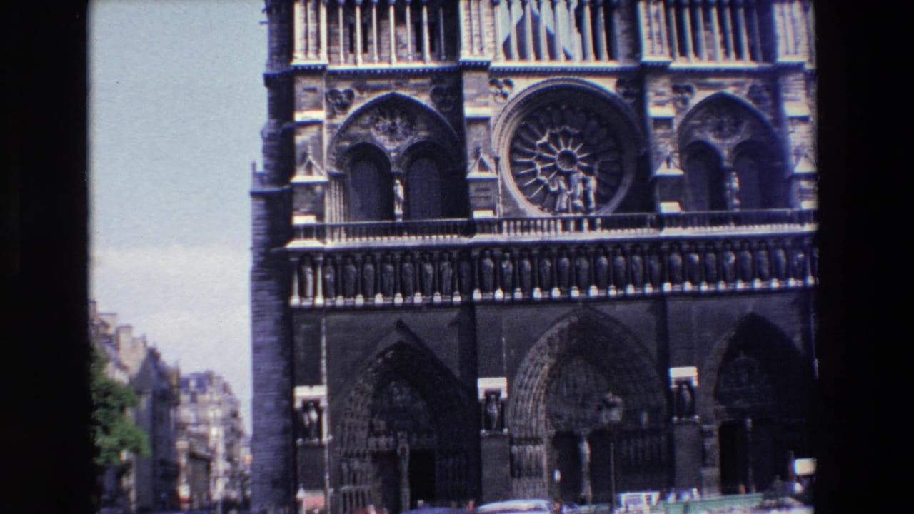 1969 8mm frame of Notre Dame Cathedral in Paris, showing the western facade, rose window, arched portals, sculptural stonework, and a narrow view of the street below.
