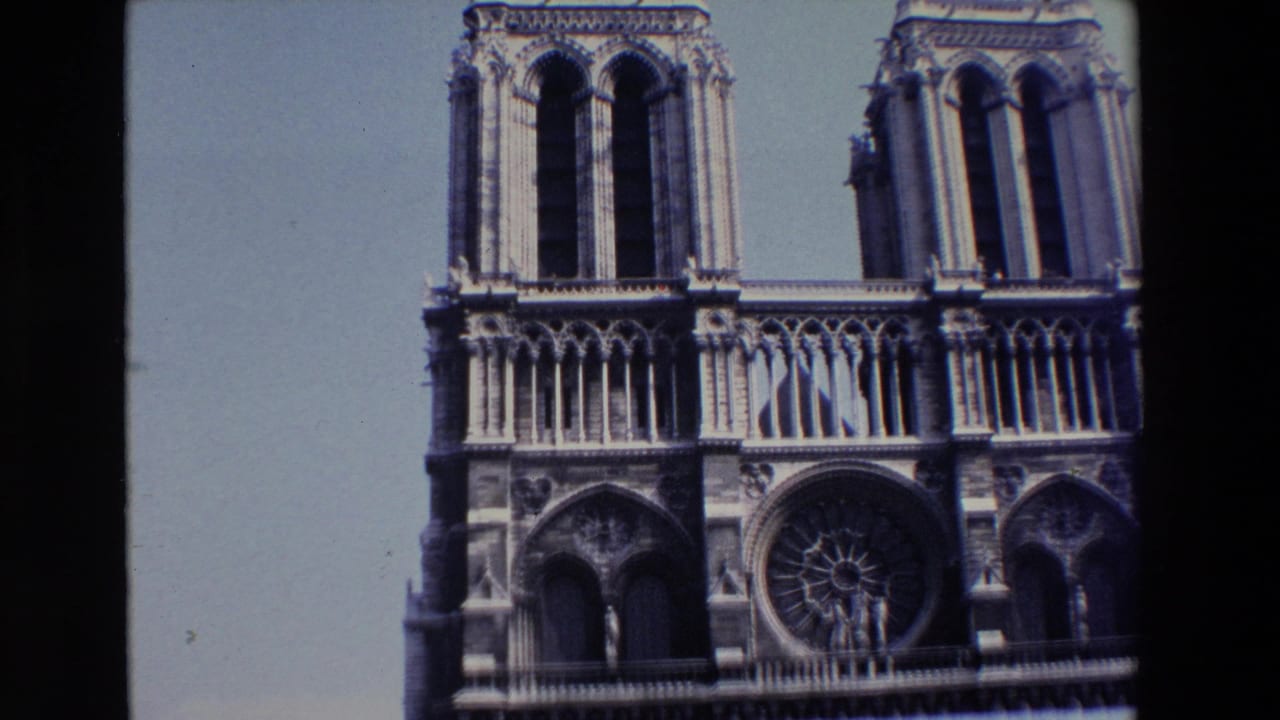1969 8mm Paris travel frame showing Notre Dame Cathedral's west facade with twin towers, Gothic arches, and the central rose window under a bright sky.