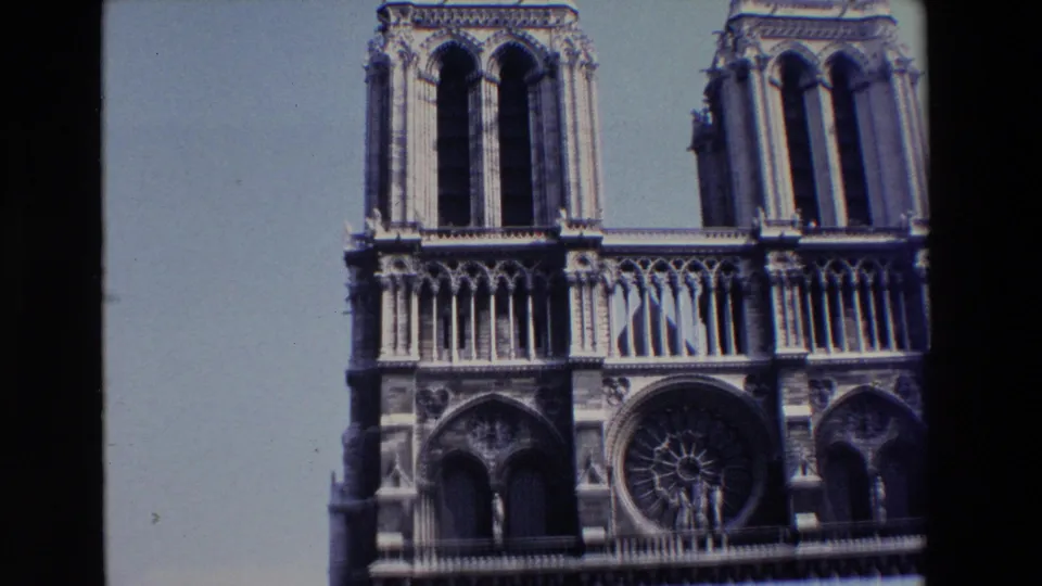 1969 8mm Paris travel frame showing Notre Dame Cathedral's west facade with twin towers, Gothic arches, and the central rose window under a bright sky.