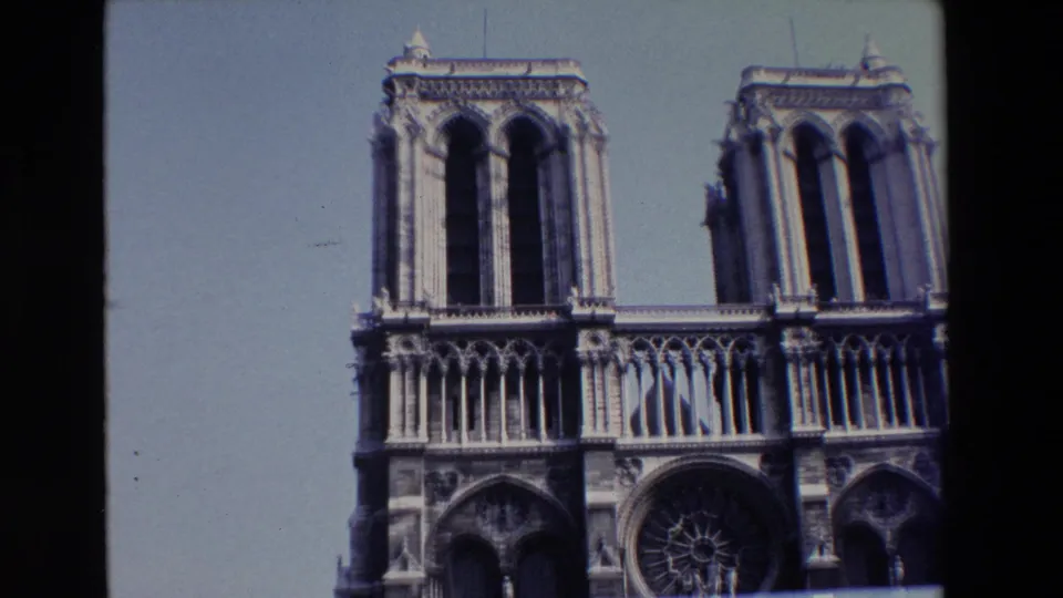 Paris home-movie frame of Notre Dame's front facade, with the towers, upper arcade, and rose window partly cropped by the film frame.