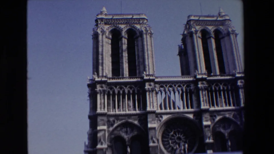 Final 1969 Paris frame showing Notre Dame's west front with its towers, rose window, Gothic portals, blue sky, and visible 8mm film border.