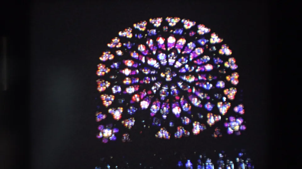 1969 Paris frame focused on Notre-Dame Cathedral's rose window, with purple, blue, red, and white stained glass glowing in darkness.
