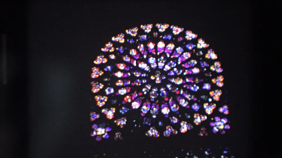 1969 Paris home-movie frame showing a centered Notre-Dame rose window with colorful stained glass radiating across a mostly dark field.