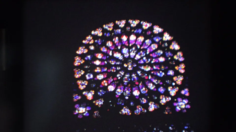 1969 Paris frame showing Notre-Dame Cathedral's rose window in close view, with saturated stained-glass colors standing out against deep shadow.