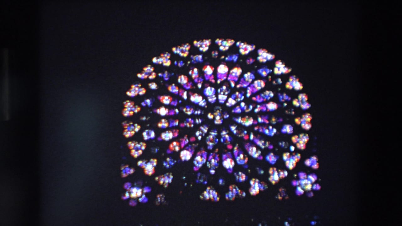 A circular rose window with blue, purple, red, and white stained glass glows against a dark Paris church interior in 1969 8mm footage.