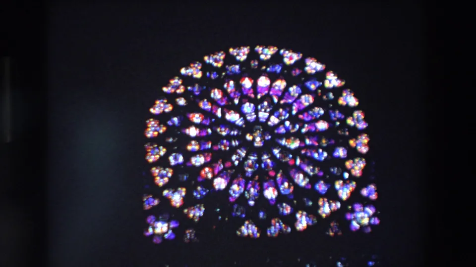 A circular rose window with blue, purple, red, and white stained glass glows against a dark Paris church interior in 1969 8mm footage.