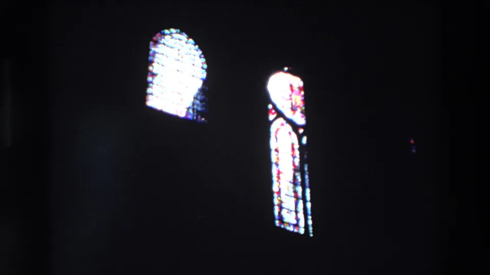 A dark church interior frames two glowing arched stained-glass windows, with exposure bloom and grain visible in the 1969 Paris 8mm scan.