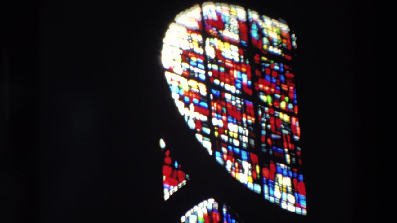 Supported Paris 1969 home-movie frame with a bright stained glass window isolated against a nearly black church interior.