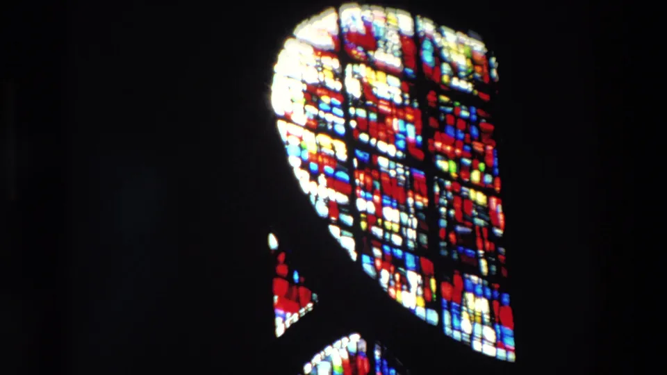Supported Paris 1969 home-movie frame with a bright stained glass window isolated against a nearly black church interior.