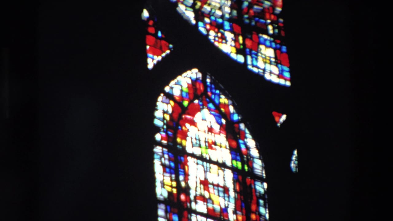 A 1969 Paris 8mm frame shows an arched stained glass window with red, blue, yellow, and white panes glowing against a nearly black church interior.