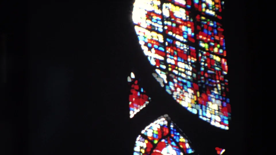 A 1969 Paris 8mm frame captures partial stained glass patterns near the top and right edges, with most of the church interior falling into shadow.