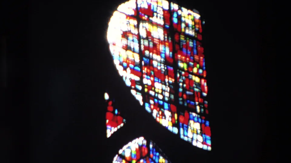 A 1969 Paris 8mm frame shows a closer portion of a stained glass window, with saturated red, blue, yellow, and white shapes surrounded by deep interior darkness.