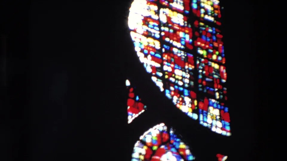 A 1969 Paris 8mm frame shows cropped arched stained glass panels along the right side, their bright multicolored panes standing out against black interior space.