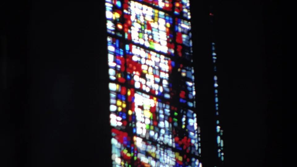 Large stained-glass window in a dark Paris church interior, filmed on 8mm in 1969, with colored panes partly obscured by a deep black vertical structure.