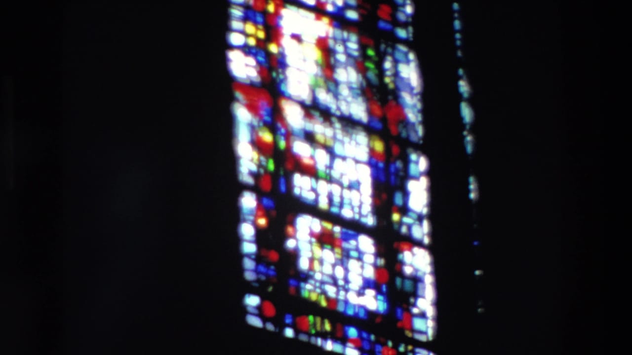 Bright stained glass panel partly framed by dark interior shadows.