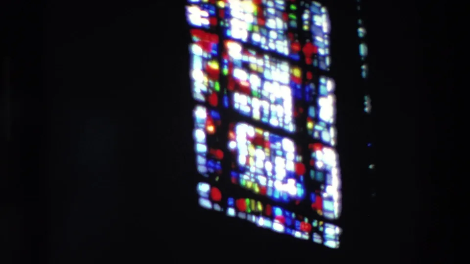 The stained glass window shifts across the frame during a slow pan, with colored glass standing out against the dark interior.