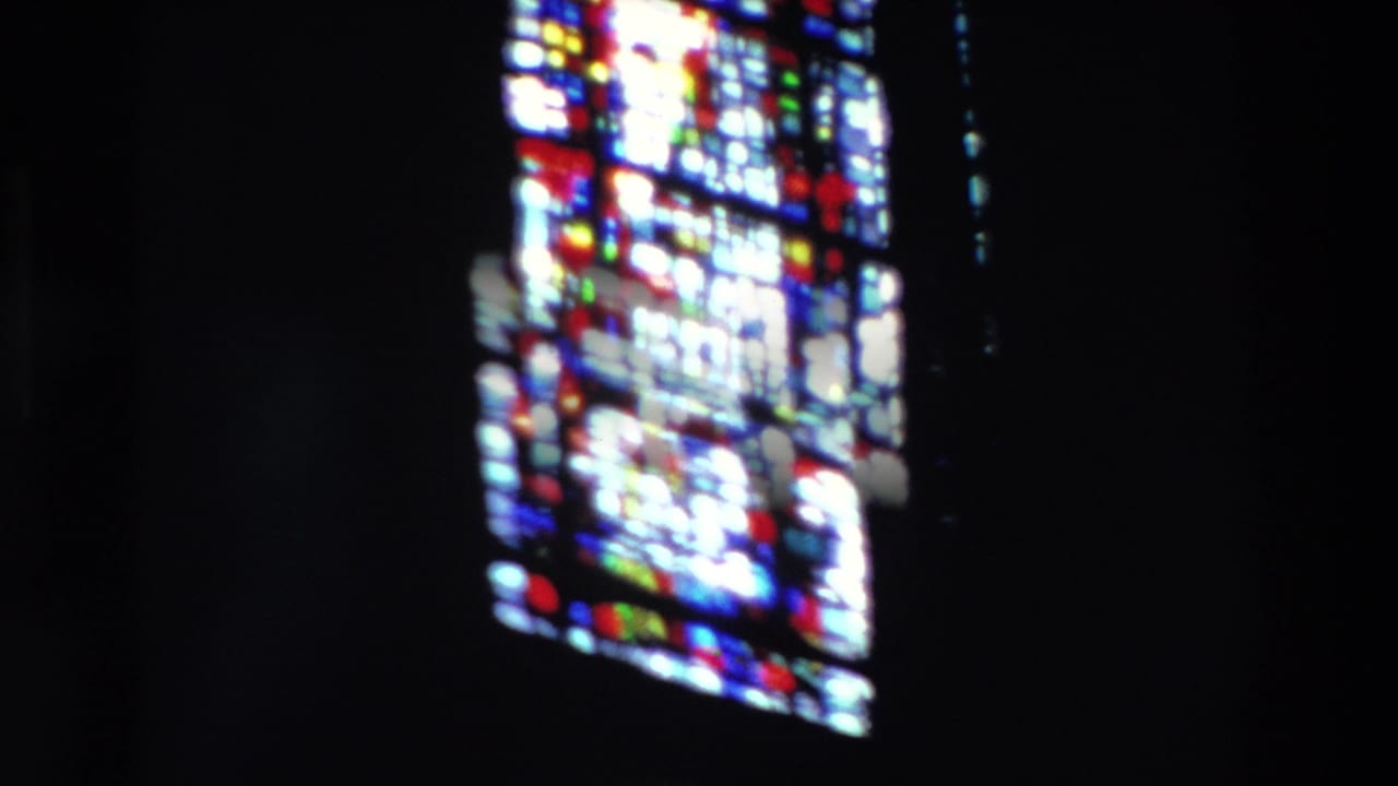1969 Paris 8mm frame showing bright stained glass panes against a nearly black church interior, with one larger window on the left and another on the right.