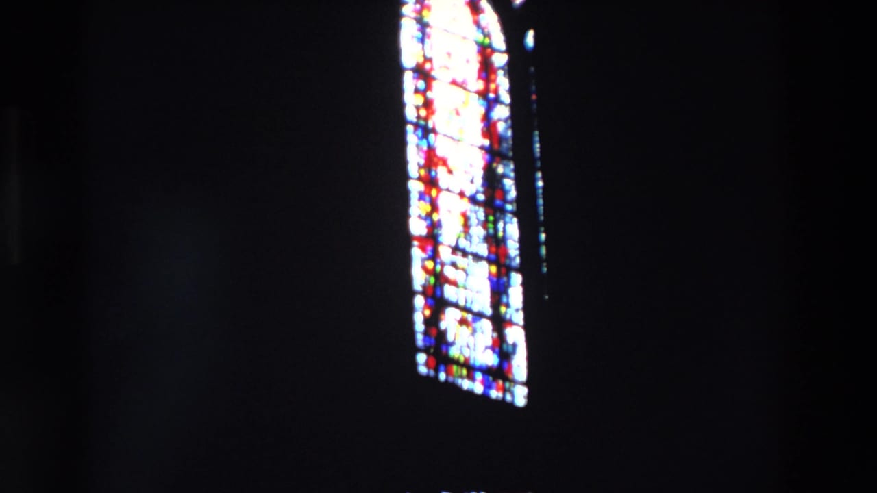 Single tall stained glass window glowing against darkness.