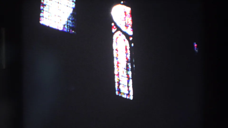 1969 Paris 8mm frame showing a tall glowing stained glass window at right, with a small upper pane and deep shadow across the church interior.