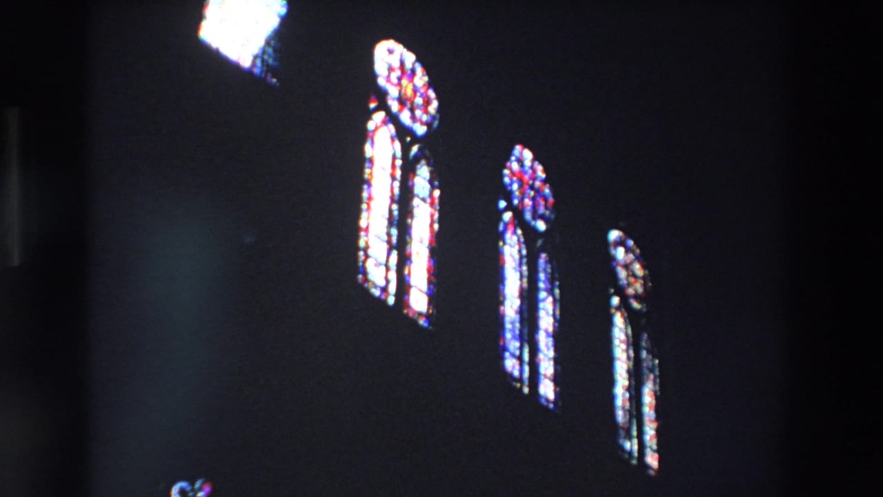Cluster of bright stained-glass windows set high in darkness.