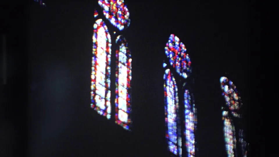 Near the end of the upward pan, the stained-glass patterns appear larger and brighter against the black interior of the Paris church.