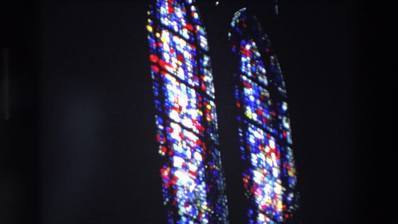 Two bright stained-glass window sections against dark church walls.