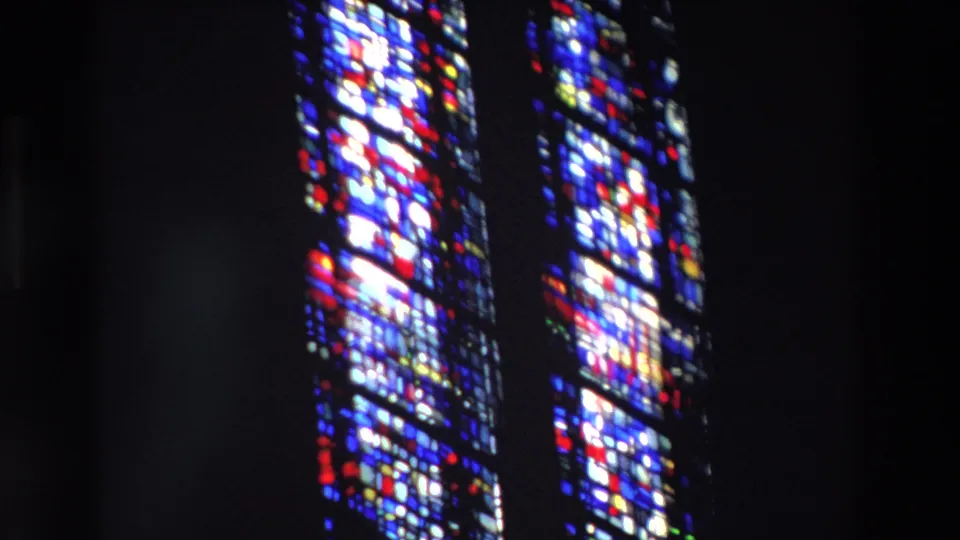 1969 Paris 8mm still showing multiple tall stained-glass windows with saturated blue and red patterns surrounded by a dim church interior.