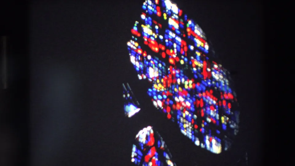 1969 Paris 8mm frame showing a large patterned stained glass section, bright red and blue glass, and small yellow highlights in a dim religious interior.