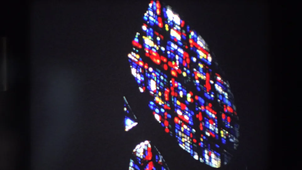 The final 1969 Paris frame holds on glowing stained glass fragments and saturated red, blue, white, and yellow light within a shadowed church-like setting.