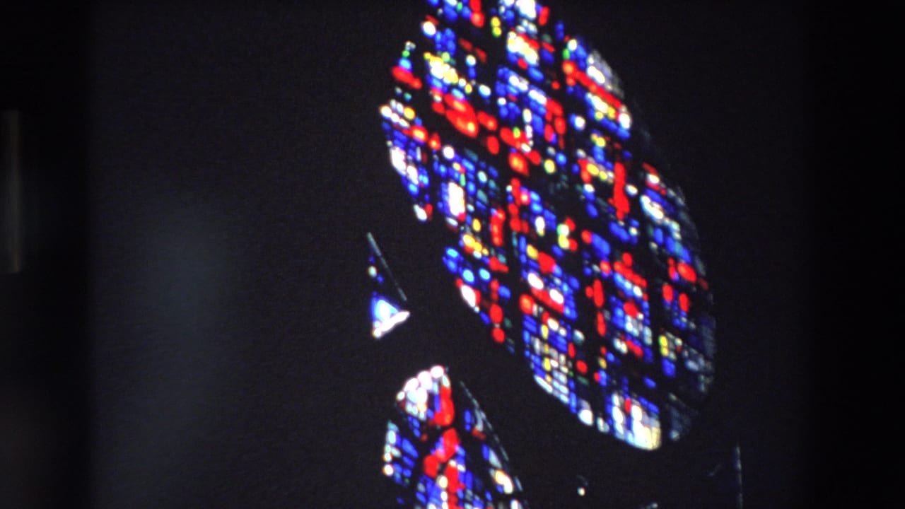 1969 Paris church interior footage shows angled sections of vivid red, blue, and white stained glass against deep shadow.