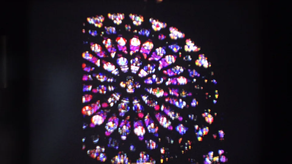 The 8mm frame centers a large multicolored rose window inside a Paris church, with dark surrounding architecture and visible film softness.