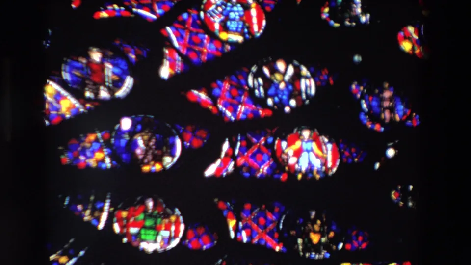 Tight Paris 1969 stained glass detail with small depicted figures, red and blue patterned panes, green accents, and dark structural leading.