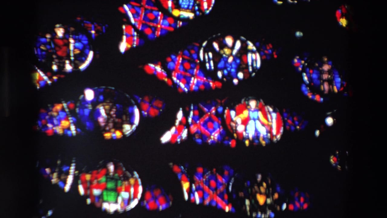 1969 Paris 8mm frame showing a close, dark view of backlit stained glass with small religious figures, circular medallions, and red-blue geometric patterns.