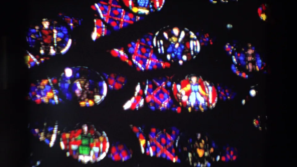 1969 Paris 8mm frame showing a close, dark view of backlit stained glass with small religious figures, circular medallions, and red-blue geometric patterns.