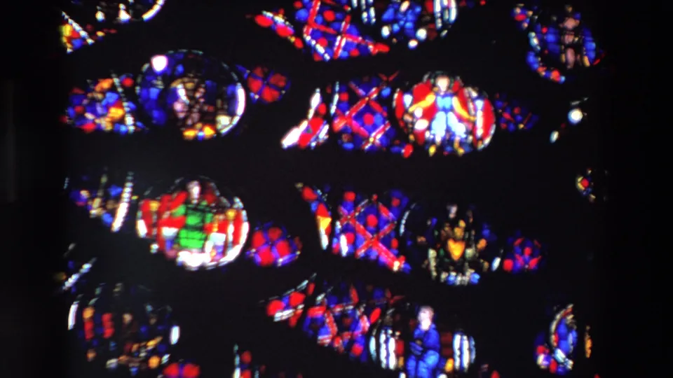 1969 Paris 8mm still showing repeated stained glass forms, including a green-robed religious figure and vivid patterned glass under low interior light.