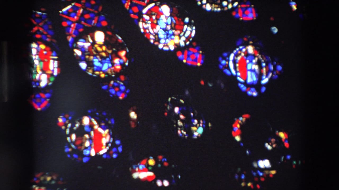 1969 Paris 8mm frame showing red, blue, and white stained glass shapes suspended in a dark church-window view.