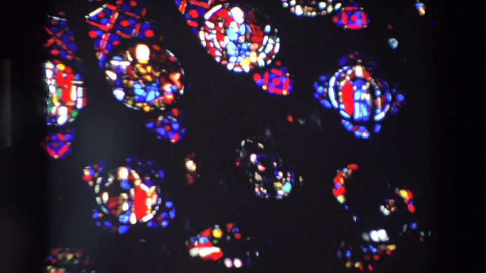 1969 Paris 8mm frame showing red, blue, and white stained glass shapes suspended in a dark church-window view.
